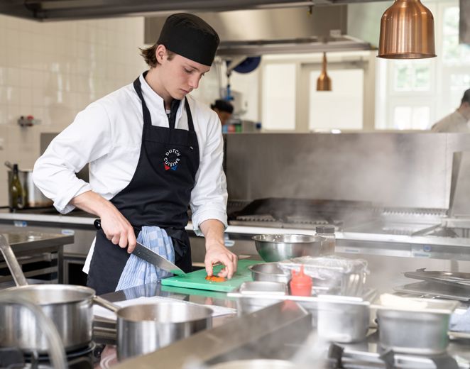 Student zelfstandig werkend kok snijdt groenten in keuken