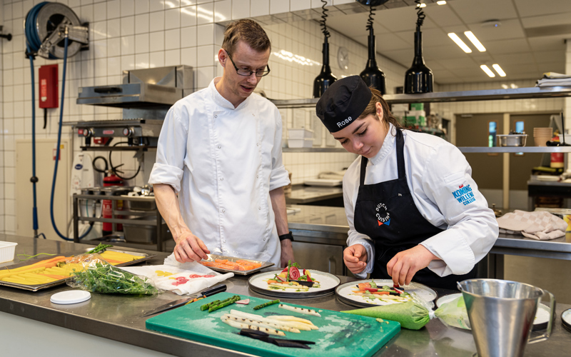 Student horeca bereidt samen met docent gerechten in de keuken